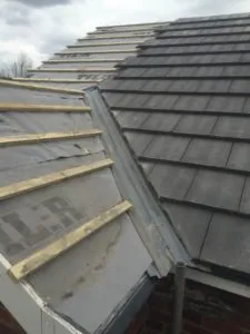 The roof of a house with a broken shingled roof.